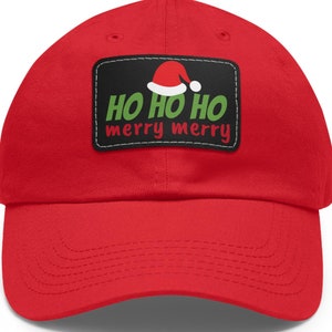 May include: A red baseball cap with a curved brim. The cap features a rectangular patch with the words "HO HO HO merry merry" in green and white, and a Santa hat graphic.