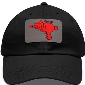 Op de afbeelding: Zwarte baseballpet met een rode en grijze patch met een cartoon-stralenpistool.