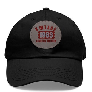 May include: Black baseball cap with a circular patch. The patch reads "VINTAGE 1963 LIMITED EDITION" in red and white lettering on a grey background. The cap has a curved peak and a rounded crown.