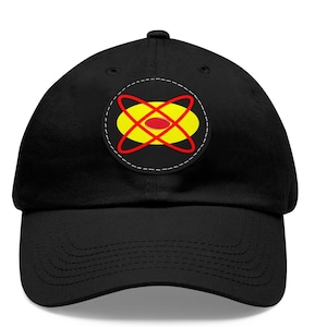 Puede incluir: Gorra de béisbol negra con visera curva. La gorra presenta un parche circular con un óvalo amarillo, líneas rojas que se cruzan y un punto rojo en el centro, delineado con costuras blancas.