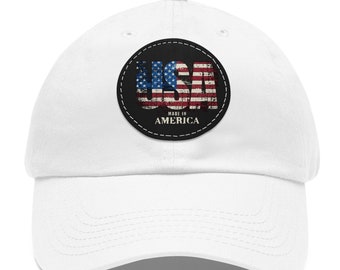 May include: White baseball cap with a black and white circular patch featuring the word "USA" in red, white, and blue with a distressed American flag design. The patch also includes the text "Made in America".