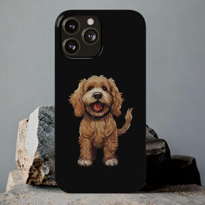 Könnte beinhalten: Schwarze Handyhülle mit einer Cartoon-Illustration eines braunen und weißen Cavapoo-Hundes. Der Hund lächelt mit herausgestreckter Zunge. Die Handyhülle hat eine glänzende Oberfläche und einen Kameraausschnitt.