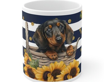 Op de afbeelding: Een witte keramische koffiemok met een blauw-wit gestreept patroon en gouden stippen. Een zwart-bruine teckelpuppy zit in een rieten mand met zonnebloemen rond de mand.