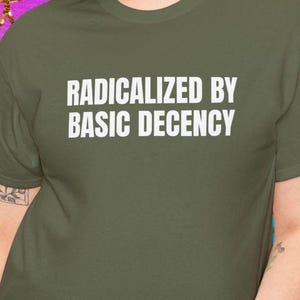 May include: A person wearing a green t-shirt with the text "Radicalized by Basic Decency" printed in white.