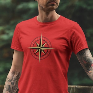 May include: A red t-shirt with a gold compass design on the front. The compass has a black outline and a red center.