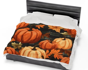 May include: A blanket featuring a fall-themed design with orange pumpkins and autumn leaves on a black and gray plaid background. The blanket is draped over a bed with a black headboard and white bedding.