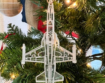 Peut inclure: Une décoration de Noël en plastique transparent en forme d'avion de chasse, suspendue à un sapin de Noël.