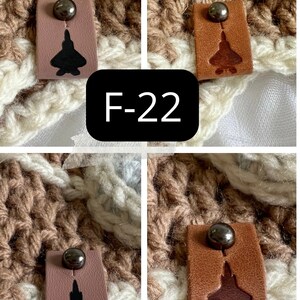 May include: Two sets of brown leather tags with a black metal button and a silhouette of a fighter jet. The tags are labeled "F-22" and "F-35".