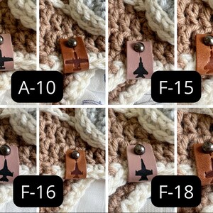 May include: Close-up of four crocheted squares with leather patches featuring different fighter jet silhouettes. The patches are labeled A-10, F-15, F-16, and F-18.