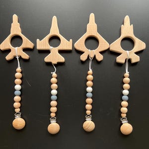 May include: Four wooden airplane teethers with silicone beads and clips. The airplanes are natural wood and the beads are brown and gray.