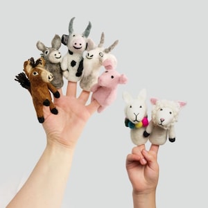 May include: A collection of felt finger puppets in the shape of farm animals, including a brown donkey, a gray donkey, a cow, a goat, a pink pig, a white rabbit with a colorful scarf, and a sheep. The puppets are held up by two hands.