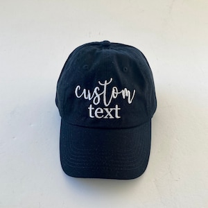 May include: A black baseball cap with white embroidery that says "custom text".