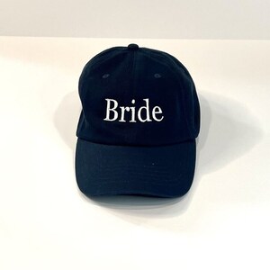 May include: A black baseball cap with the word "Bride" embroidered in white on the front.