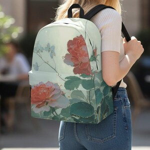 May include: A backpack featuring a light green background with a floral pattern of large red and pink roses and green leaves. The bag has black shoulder straps and a main compartment with a zipper closure, displaying a botanical art design.