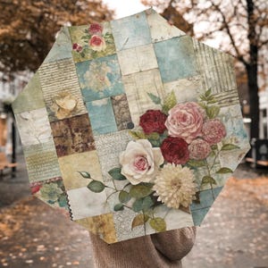 May include: An open umbrella with a patchwork design of squares in shades of blue, green, and tan. The umbrella features a floral arrangement of roses and dahlias in shades of red, pink, and cream. The umbrella is held open.