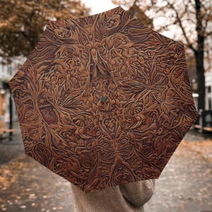 May include: Brown umbrella with a detailed, embossed floral pattern. The umbrella's design features a complex arrangement of leaves and organic shapes, creating a textured appearance. The umbrella is open, and the handle is not visible.