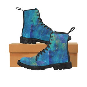 May include: A pair of blue combat boots with a colorful abstract design. The boots have black soles, black laces, and a pull tab at the back. The boots are displayed on a brown cardboard box.