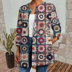 May include: A long, open-front crochet jacket featuring a patchwork design with floral motifs in shades of blue, red, pink, and orange. The jacket has three-quarter sleeves and pockets. The person is wearing blue jeans and a white top.