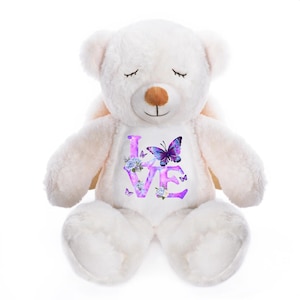 May include: A white plush teddy bear with the word "LOVE" in purple script on its chest. The word is decorated with blue flowers and purple butterflies. The bear has closed eyes and a brown nose.