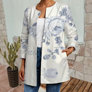 Può includere: Una giacca bianca aperta con un grande motivo floreale nei toni del grigio e del blu. La giacca ha maniche lunghe e tasche. Il motivo floreale copre la parte anteriore e le maniche. La giacca è indossata sopra un top bianco e jeans blu.