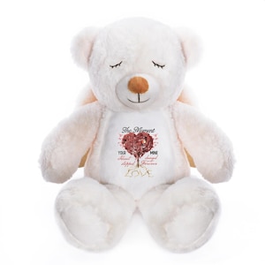 May include: A white plush teddy bear with closed eyes and small wings. The bear has a brown nose and a heart-shaped tree design on its chest with the words "The Moment Your Heart Stopped Forever".