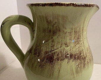 May include: A green ceramic pitcher with a brown glaze. The pitcher has a wide mouth and a handle.