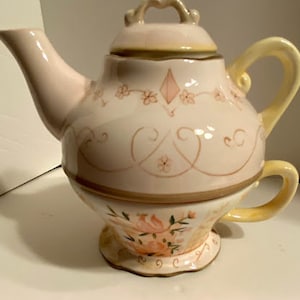 May include: A white ceramic teapot with a floral design and a matching teacup. The teapot has a lid and a handle. The teacup has a handle and a saucer.