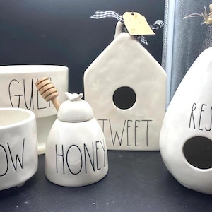 Puede incluir: Colección de artículos de decoración para el hogar de cerámica blanca. Incluye una maceta pequeña con el texto "GROW", un tarro de miel, una casa para pájaros con el texto "TWEET", una jardinera con el texto "GUL" y una casa para pájaros en forma de pera con el texto "REST".