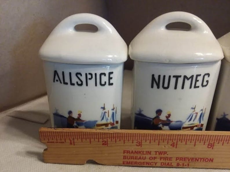 May include: Set of three white ceramic spice jars with blue and white illustrations. The jars are labelled "Allspice", "Nutmeg", and "Cinnamon".