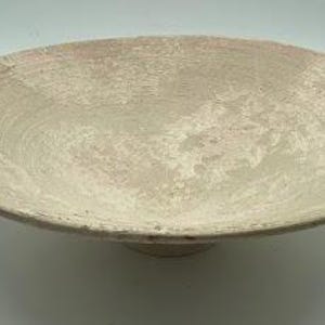 Könnte beinhalten: Eine große, cremefarbene Keramikschale mit einem breiten, flachen Boden und einem leicht erhöhten Rand. Die Schale hat eine strukturierte, marmorierte Oberfläche mit einem dezenten Rosaton.