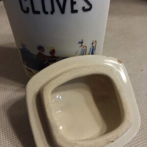 May include: White ceramic jar with a lid. The jar has a blue and white design and the word "CLOVES" printed on the front.