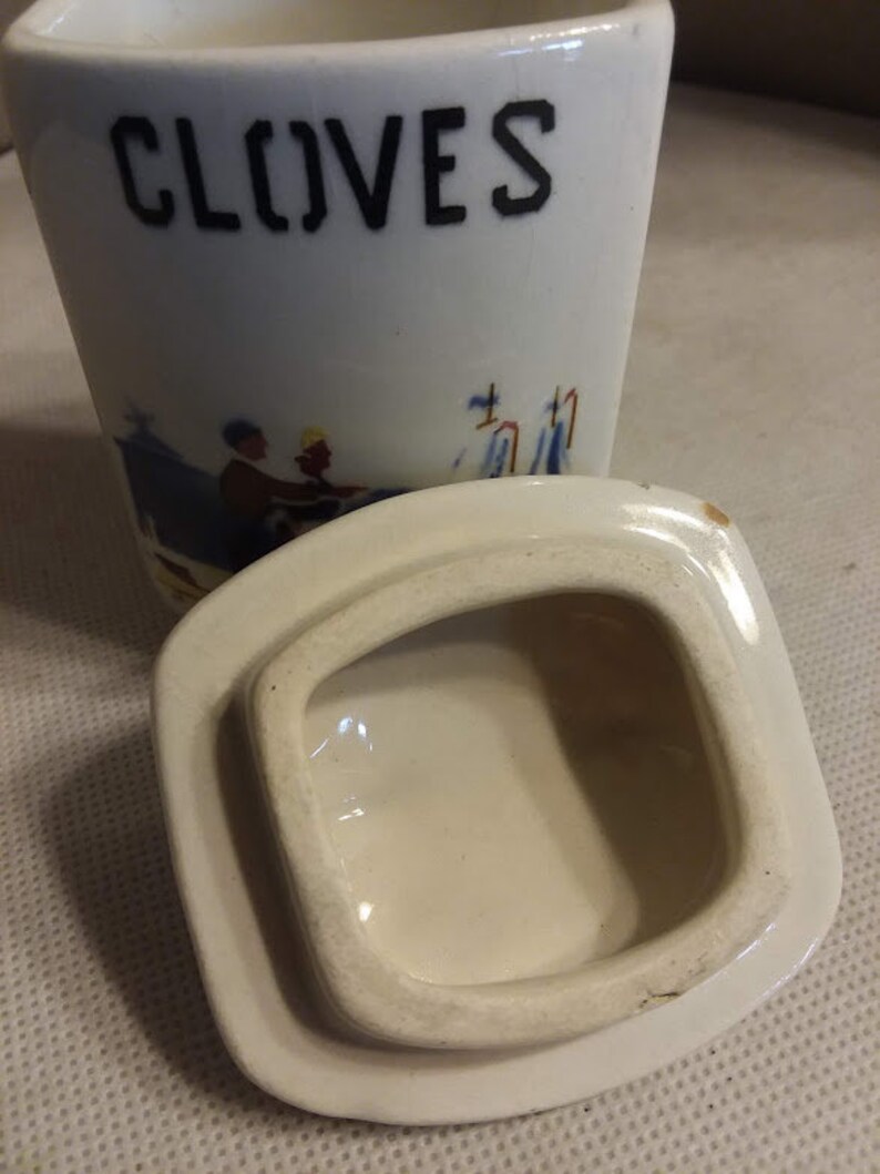 May include: White ceramic jar with a lid. The jar has a blue and white design and the word "CLOVES" printed on the front.