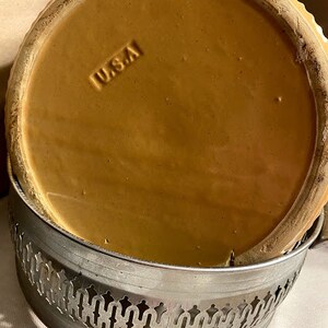 May include: A brown ceramic pie plate with a scalloped edge and a silver metal base. The base has a decorative design and the plate has the word "USA" stamped on the bottom.