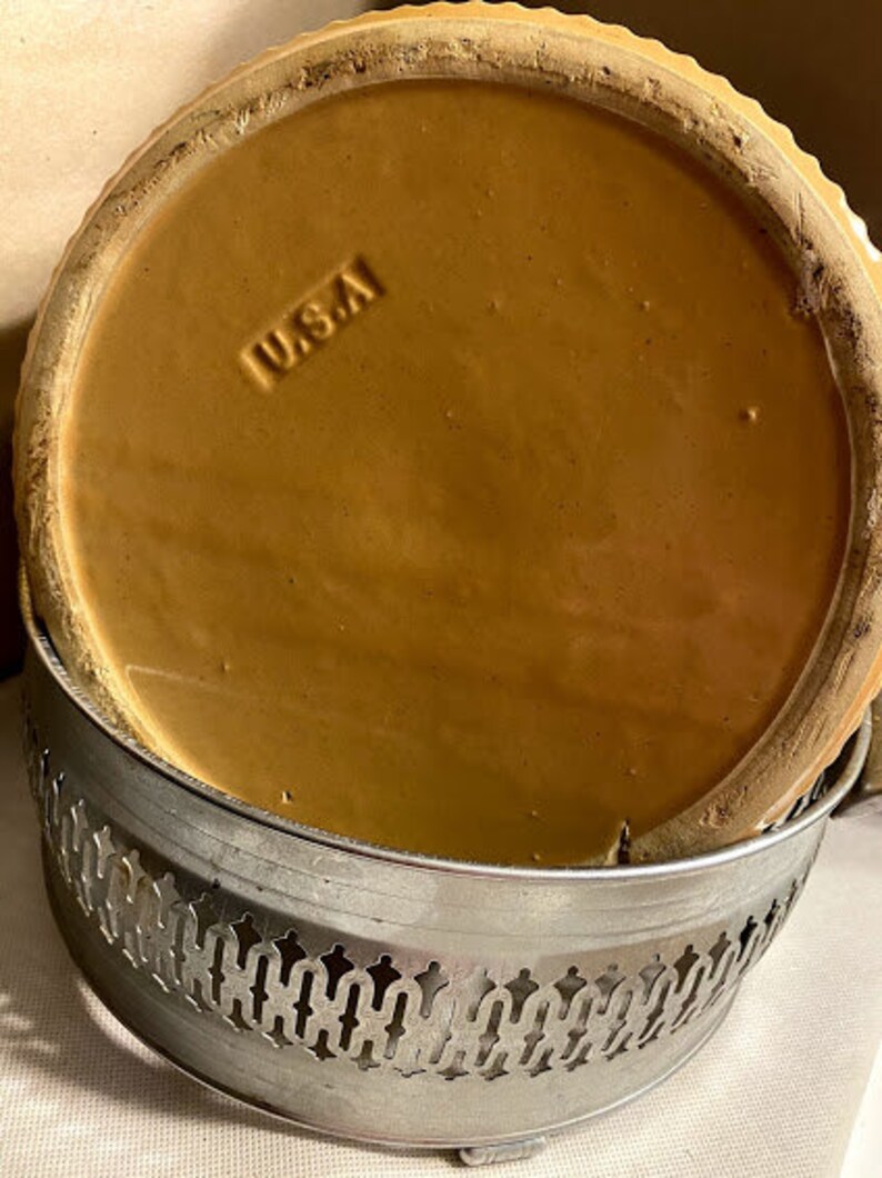 May include: A brown ceramic pie plate with a scalloped edge and a silver metal base. The base has a decorative design and the plate has the word "USA" stamped on the bottom.