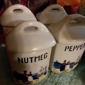May include: Four white ceramic spice jars with lids and handles. The jars are decorated with blue and white illustrations and have the words "Nutmeg" and "Pepper" printed on them.