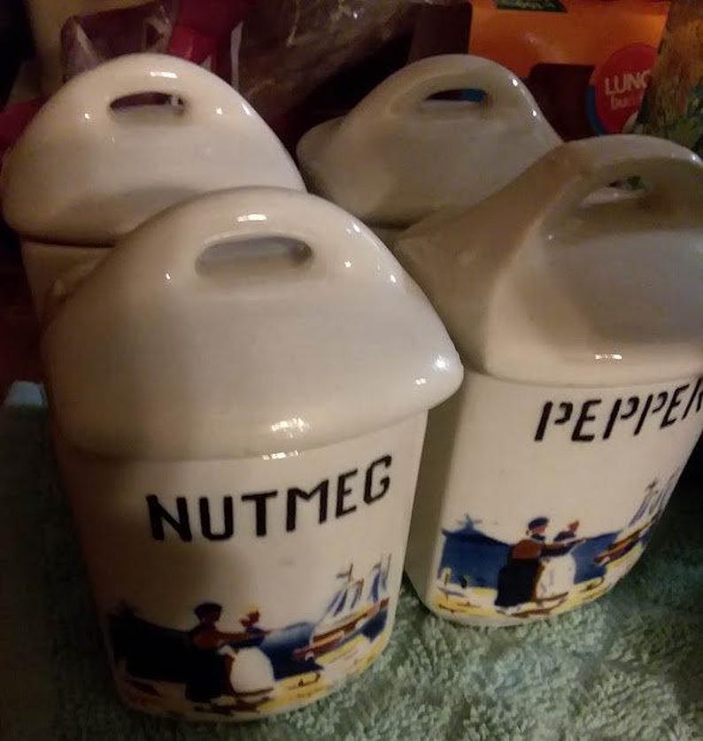 May include: Four white ceramic spice jars with lids and handles. The jars are decorated with blue and white illustrations and have the words "Nutmeg" and "Pepper" printed on them.