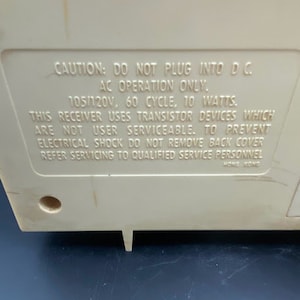 May include: A white plastic device with a warning label that reads "CAUTION: DO NOT PLUG INTO DC. AC OPERATION ONLY. 105/120V, 60 CYCLE. 10 WATTS. THIS RECEIVER USES TRANSISTOR DEVICES WHICH ARE NOT USER SERVICEABLE. TO PREVENT ELECTRICAL SHOCK DO NOT REMOVE BACK COVER REFER SERVICING TO QUALIFIED SERVICE PERSONNEL HONG KONG"