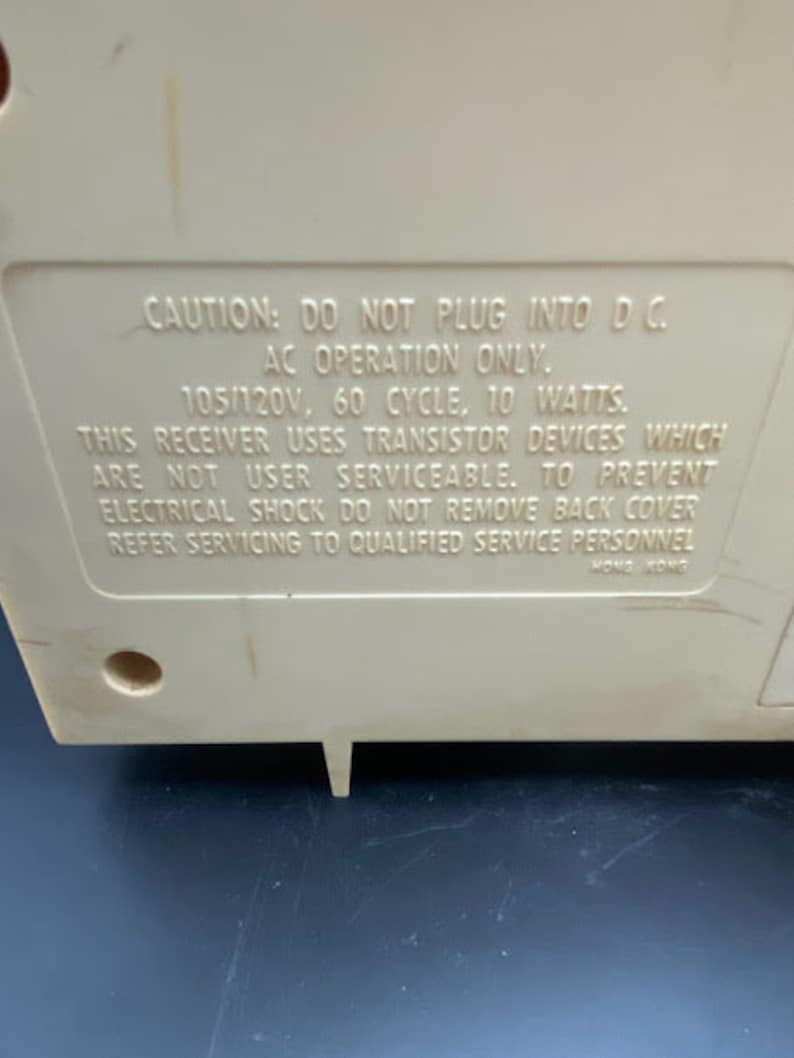 May include: A white plastic device with a warning label that reads "CAUTION: DO NOT PLUG INTO DC. AC OPERATION ONLY. 105/120V, 60 CYCLE. 10 WATTS. THIS RECEIVER USES TRANSISTOR DEVICES WHICH ARE NOT USER SERVICEABLE. TO PREVENT ELECTRICAL SHOCK DO NOT REMOVE BACK COVER REFER SERVICING TO QUALIFIED SERVICE PERSONNEL HONG KONG"