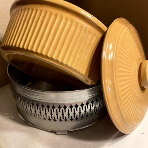 May include: A set of two vintage ceramic casserole dishes with a yellow glaze. The dishes have a fluted design and are stacked on top of each other. The bottom dish has a metal base with a decorative design.