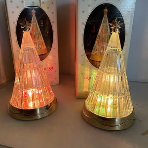 May include: Two glass Christmas tree lamps with gold bases and white boxes. The boxes have a star design and the text "Crystal Tree" and "Holiday Tree".