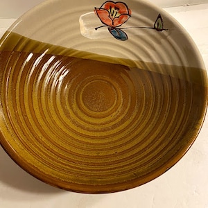 Puede incluir: Un tazón de cerámica marrón y blanco con un diseño floral. El tazón tiene un interior marrón y un exterior blanco con un borde marrón. El diseño floral es en rojo, azul y verde.