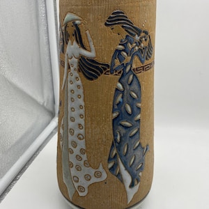 May include: A ceramic vase with a brown background and two women in white and blue dresses. The women are depicted in a stylized art style.