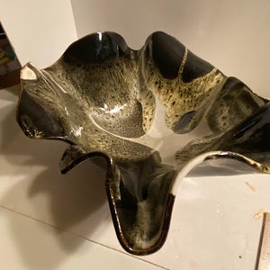 May include: A ceramic bowl with a unique, abstract design. The bowl is white with black and green accents, and has a wavy, organic shape.