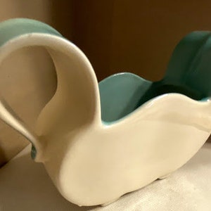 Może przedstawiać: Biała ceramiczna sosjerka z tealowym niebieskim rantem i uchwytem. Sosjerka ma unikalny, organiczny kształt.