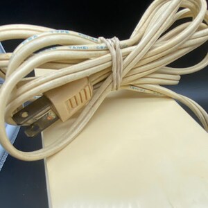 May include: Close-up of a beige electrical cord with a two-prong plug. The cord is coiled and tied with a rubber band. The cord is labelled "TYPE", "TAIWAN", and "CSA".