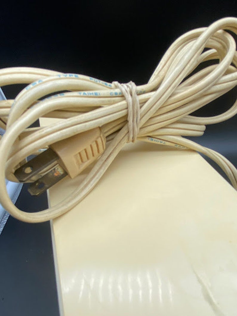 May include: Close-up of a beige electrical cord with a two-prong plug. The cord is coiled and tied with a rubber band. The cord is labelled "TYPE", "TAIWAN", and "CSA".