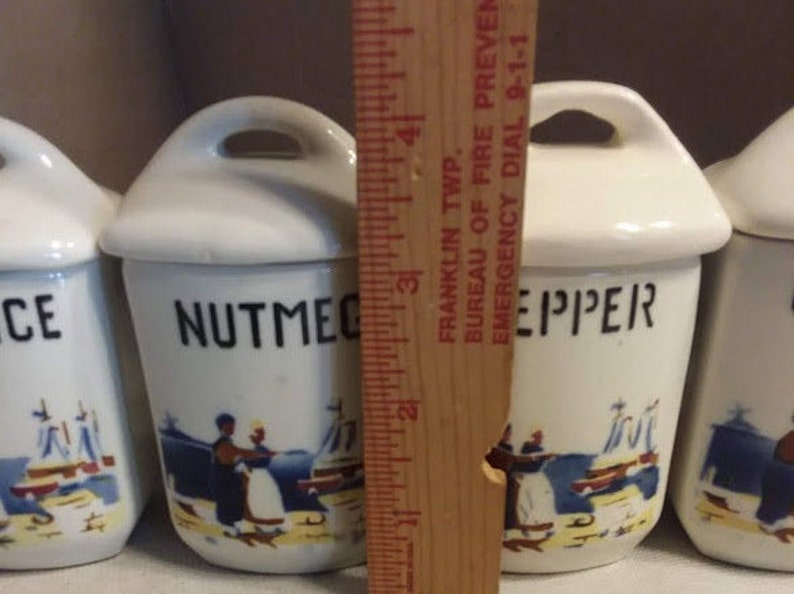 May include: Set of four white ceramic spice jars with blue and white nautical designs. The jars are labelled "Nutmeg", "Pepper", "Salt", and "Cinnamon".