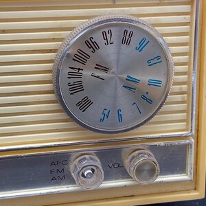 May include: A vintage cream-coloured radio with a silver dial and black lettering. The dial has numbers from 54 to 106 and the words "AM" and "FM". The radio has knobs for "AFC", "FM", "AM", "VOL" and a silver trim around the edge.