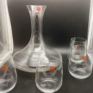 May include: A set of clear glass decanter and glasses. The decanter has a wide base and a tall, slender neck. The glasses are short and round. The set is perfect for serving wine or other beverages.