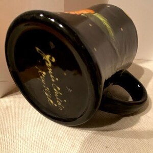 May include: Black ceramic mug with a white and yellow floral design and the text "Annie Childs,  Erie, Illinois" on the bottom.